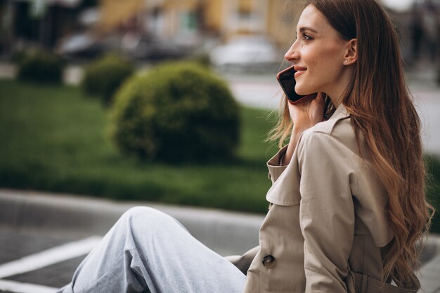 Giovane donna felice che si siede nel parco e che parla al telefono