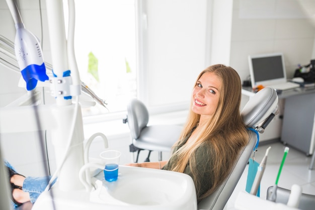 Giovane donna felice che si siede sulla sedia dentale