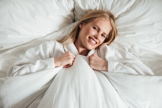 Giovane donna felice che si trova sul grande letto bianco con la coperta
