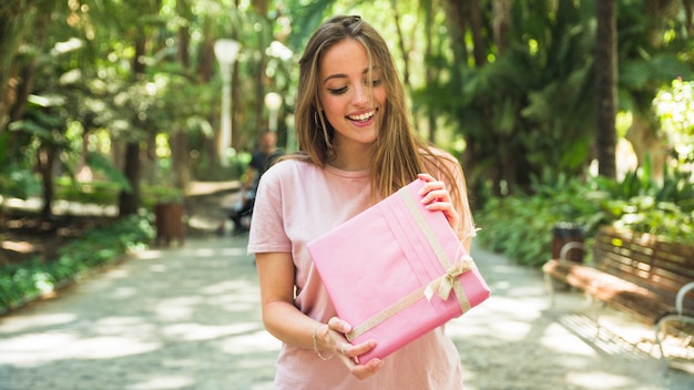 Giovane donna felice che tiene il contenitore di regalo rosa in parco