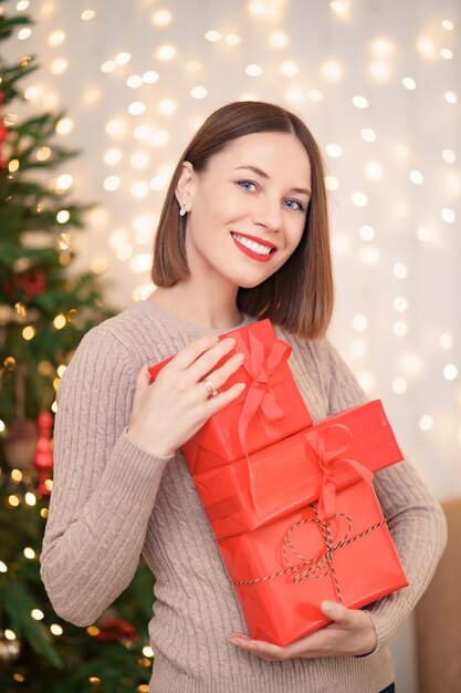 Giovane donna felice che tiene molte caselle presenti con l'albero di Natale e le luci