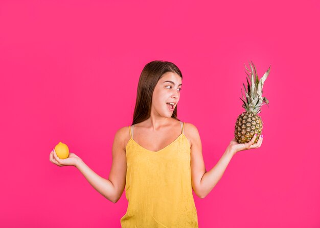Giovane donna felice con frutta esotica divertendosi su sfondo rosa