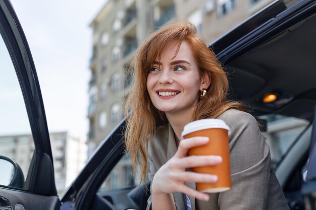 Giovane donna felice con il caffè che ha un freno nella sua macchina Vista laterale della donna con il caffè da portare in mano Giovane donna che beve caffè nella sua macchina