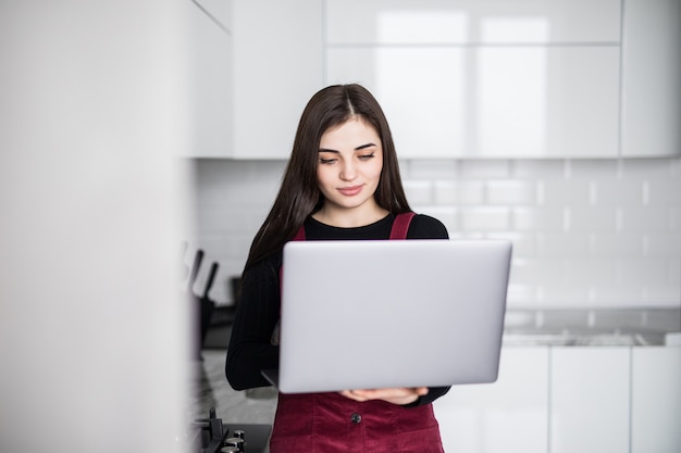 Giovane donna felice nella lettura della cucina che notizie sul suo computer portatile