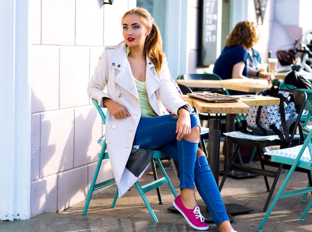 Giovane donna felice sorridente e rilassante alla terrazza del caffè della città, tempo soleggiato, trucco luminoso, abbigliamento casual elegante, vacanze, viaggi, vacanze, gioia.