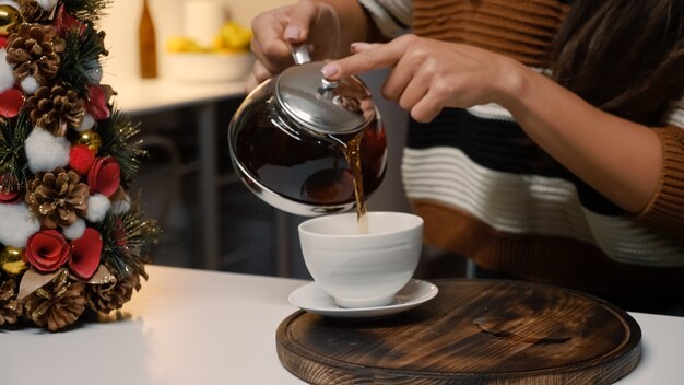 Giovane donna festosa che versa il tè dal bollitore in tazza