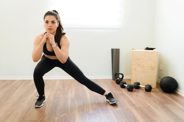 Giovane donna fitness che fa affondi laterali a casa per il suo allenamento HIIT. Donna muscolare in abbigliamento sportivo che lavora a casa