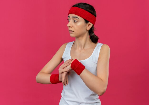 Giovane donna fitness in abiti sportivi con archetto guardando da parte preoccupato in fase di riscaldamento in piedi sopra la parete rosa