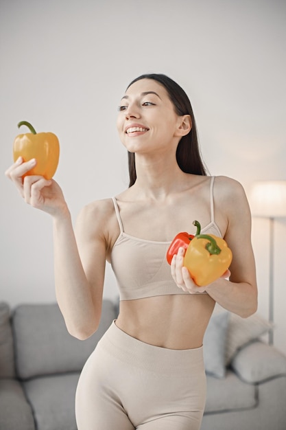 Giovane donna fitness in piedi a casa con paprika rossa e gialla