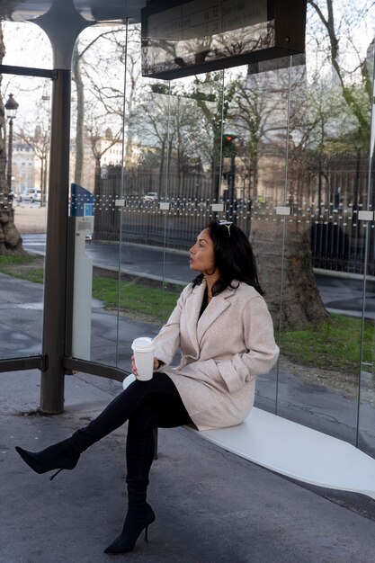 Giovane donna francese che aspetta alla stazione l'autobus e beve caffè