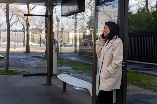 Giovane donna francese che aspetta alla stazione l'autobus e parla sullo smartphone