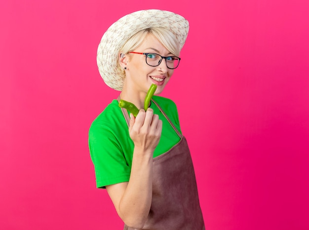 Giovane donna giardiniere con i capelli corti in grembiule e cappello che mostra le metà del peperoncino verde