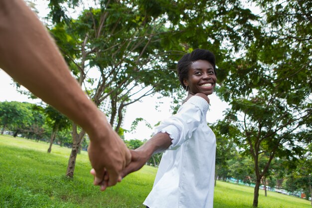 Giovane donna gioiosa che porta il suo uomo a mano nel parco