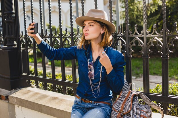 Giovane donna graziosa alla moda che prende un selfie, vestito in jeans e camicia di jeans