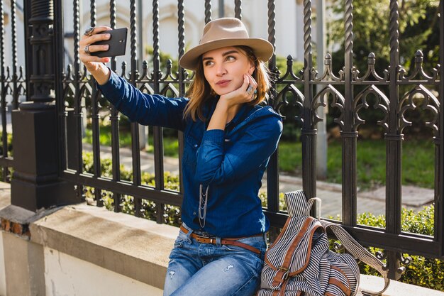 Giovane donna graziosa alla moda che prende un selfie, vestito in jeans e camicia di jeans