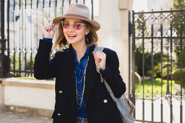 Giovane donna graziosa alla moda sorridente, stupita, sorpresa, felice, vestita in jeans e cappotto blu scuro