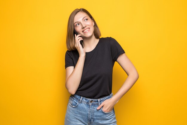 Giovane donna graziosa che comunica sul telefono delle cellule sopra la parete gialla