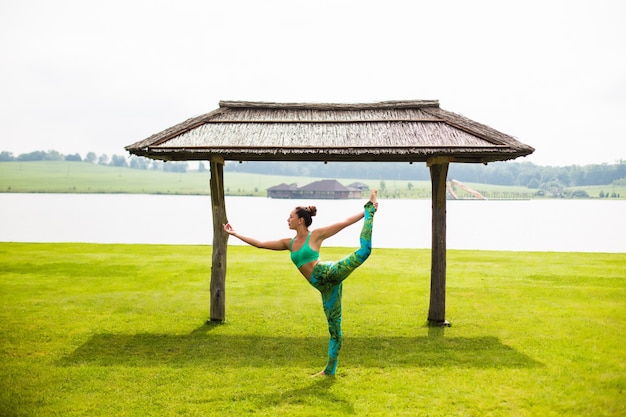 Giovane donna graziosa che fa yoga nel parco di mattina vicino al lago