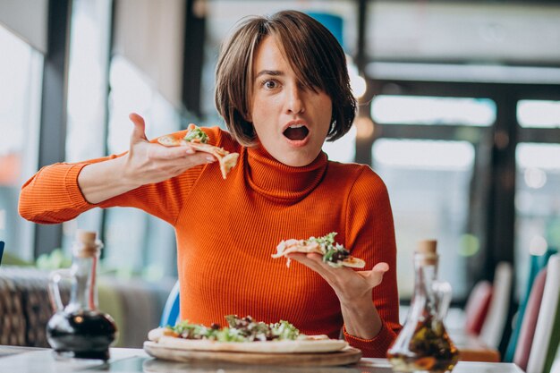 Giovane donna graziosa che mangia pizza al bar della pizza