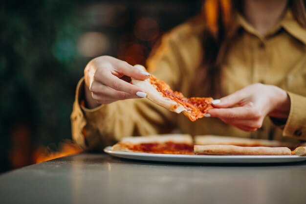 Giovane donna graziosa che mangia pizza in un bar