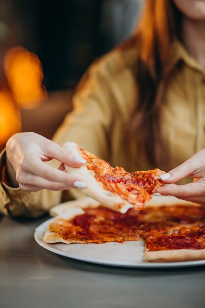 Giovane donna graziosa che mangia pizza in un bar