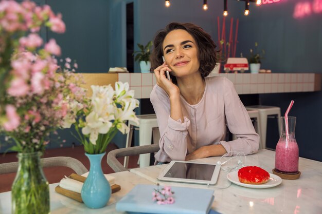 Giovane donna graziosa che parla sul telefono cellulare mentre sedendosi