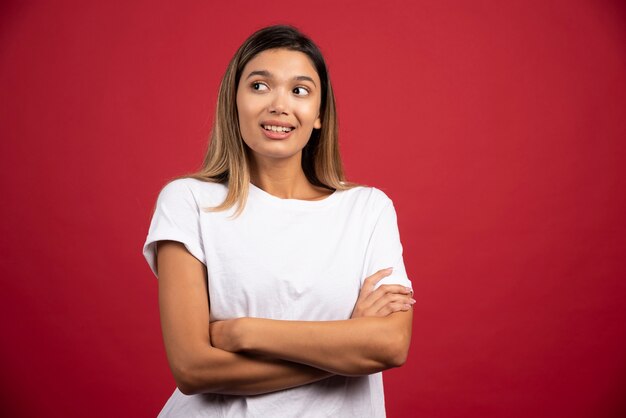 Giovane donna graziosa che posa sulla parete rossa.