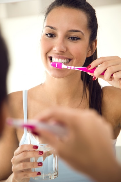 Giovane donna graziosa che pulisce i suoi denti nel bagno.