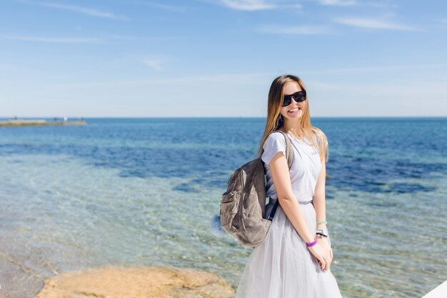 Giovane donna graziosa con i capelli lunghi è in piedi vicino al mare