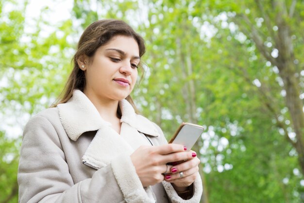 Giovane donna graziosa contenta che utilizza smartphone nel parco