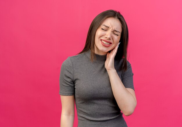 giovane donna graziosa dolorante che mette la mano sulla guancia che soffre di mal di denti con gli occhi chiusi