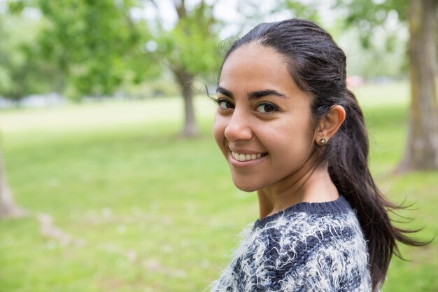 Giovane donna graziosa felice che posa alla macchina fotografica in parco