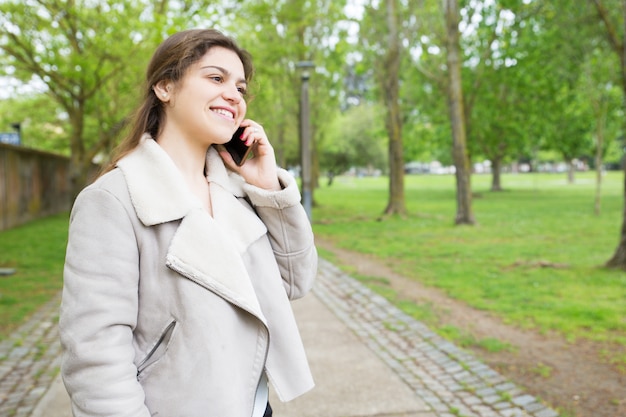 Giovane donna graziosa felice che rivolge allo smartphone in parco