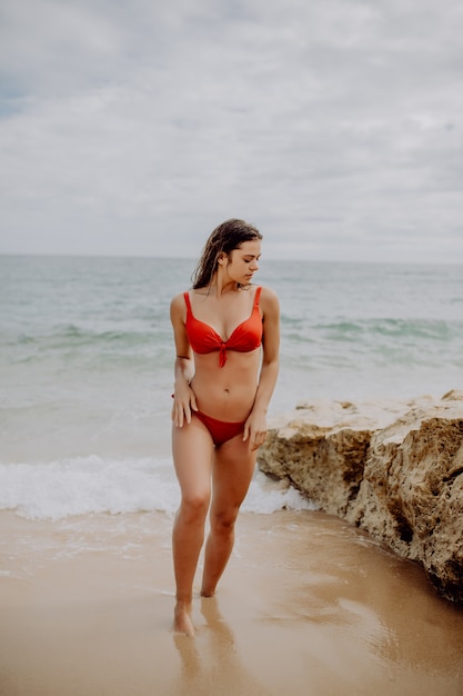 Giovane donna graziosa in bikini rosso che cammina verso l'oceano.