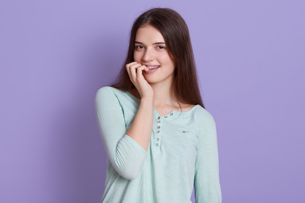 Giovane donna hared scura che porta camicia casuale che esamina macchina fotografica e che morde le sue dita