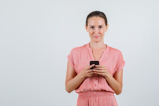 Giovane donna in abito a righe tenendo il telefono cellulare e sorridente, vista frontale.