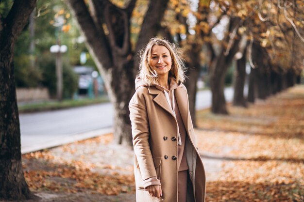 Giovane donna in abito beige fuori in un parco in autunno