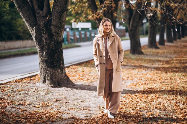 Giovane donna in abito beige fuori in un parco in autunno