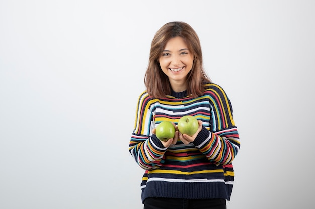 Giovane donna in abito casual in possesso di mele verdi con espressione sorridente.