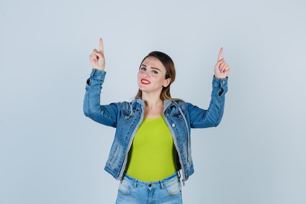 Giovane donna in abito di jeans che punta verso l'alto e sembra felice, vista frontale.