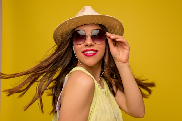 Giovane donna in abito giallo con cappello e occhiali da sole ascoltando musica