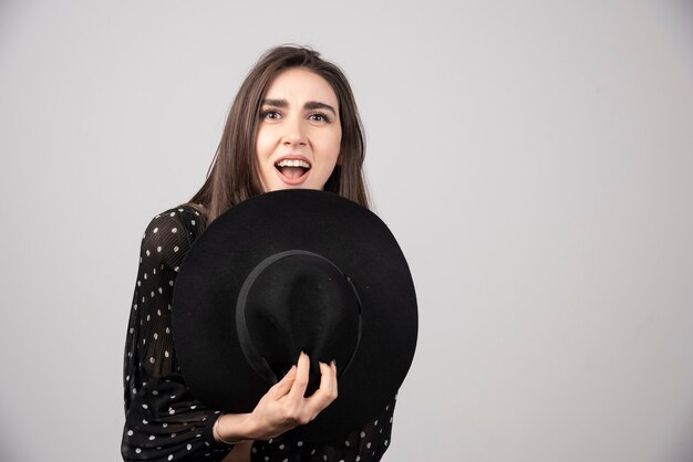 Giovane donna in abito nero tenendo il cappello contro il suo corpo.