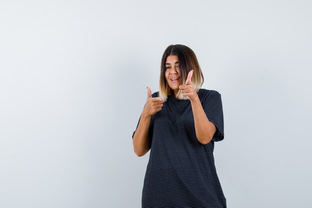 Giovane donna in abito polo che punta alla telecamera e che sembra felice, vista frontale.