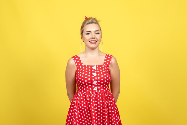 giovane donna in abito rosso a pois in piedi e sorridente sul giallo