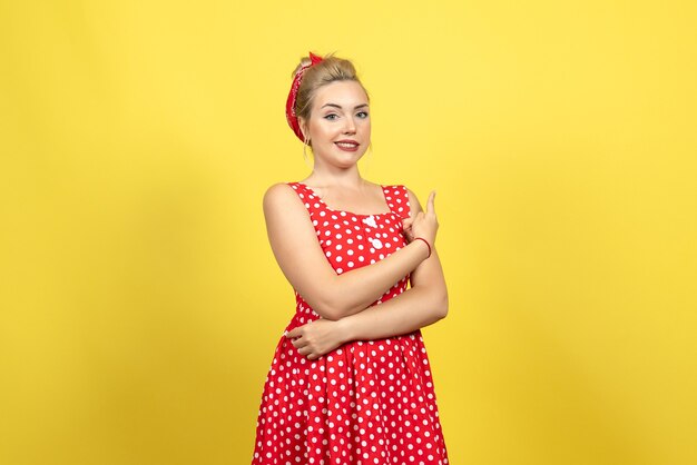 giovane donna in abito rosso a pois in posa su giallo