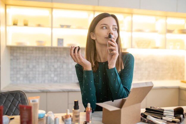 Giovane donna in abito verde che rappresenta nuovi cosmetici e che sembra soddisfatta