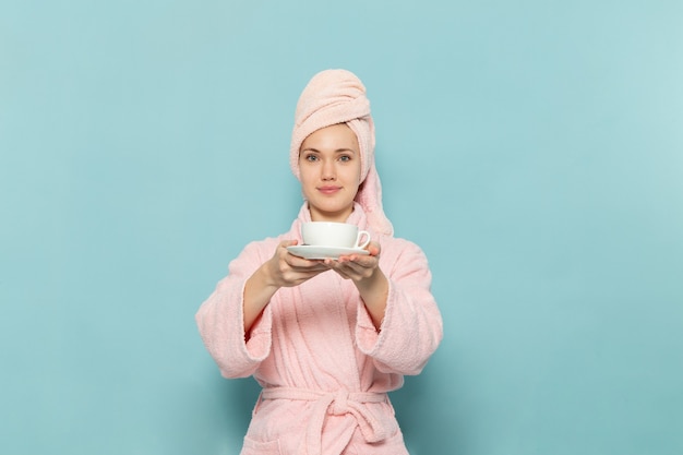 giovane donna in accappatoio rosa dopo la doccia bere caffè sorridente sul blu