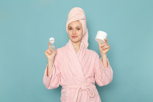 giovane donna in accappatoio rosa dopo la doccia tenendo la crema spray sul blu