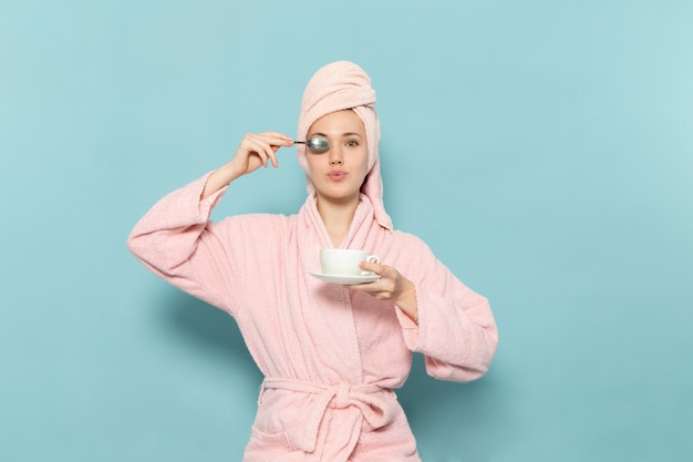 giovane donna in accappatoio rosa dopo la doccia tenendo la tazza di caffè sul blu