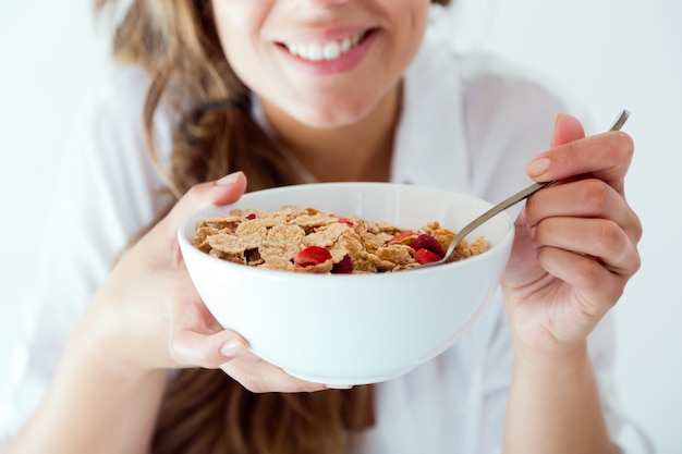 Giovane donna in biancheria intima che mangia i cereali. Isolato su bianco